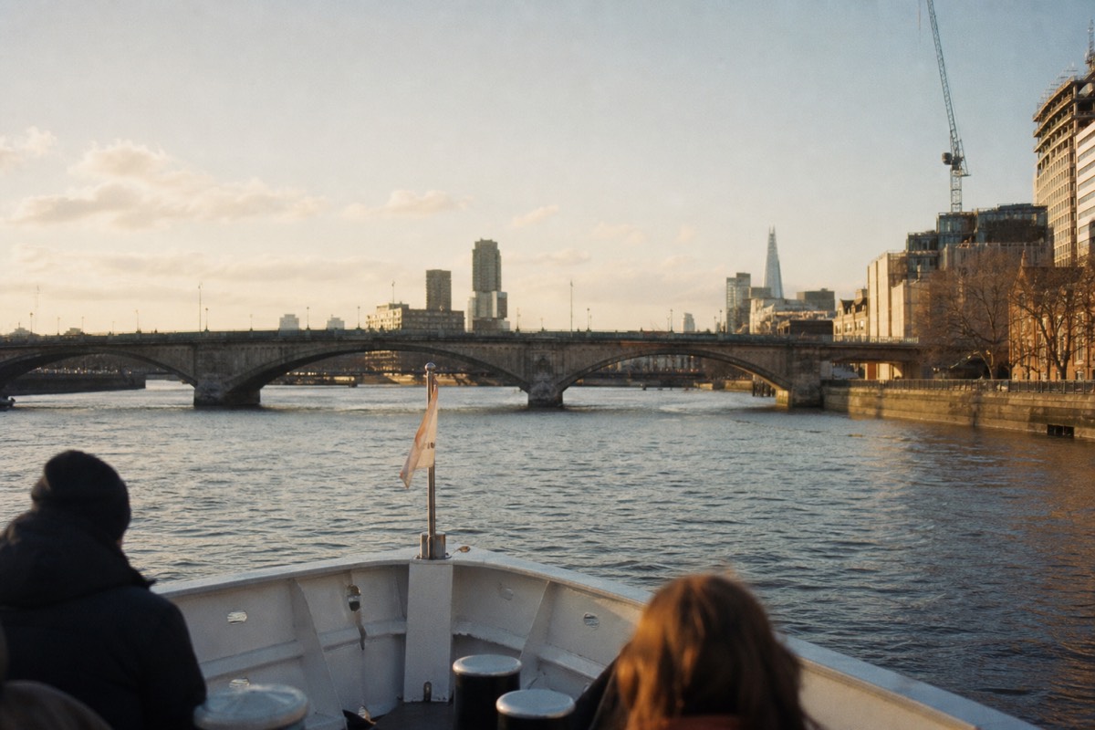 A river cruise boat's bow cutting through the Thames toward a historic bridge